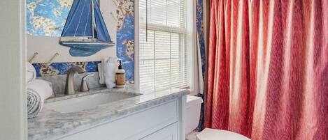 A bathroom with a nautical-themed wall, a white toilet, and a red curtain.