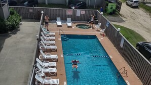 Et rektangulært swimmingpool med et springbræt, omgivet af hvide liggestole og en betonflisebelagt terrasse.