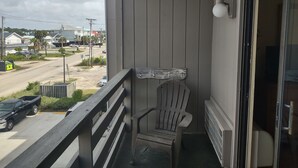 En balkon med en træstol, udsigt til en gade med biler og en bygning i baggrunden.