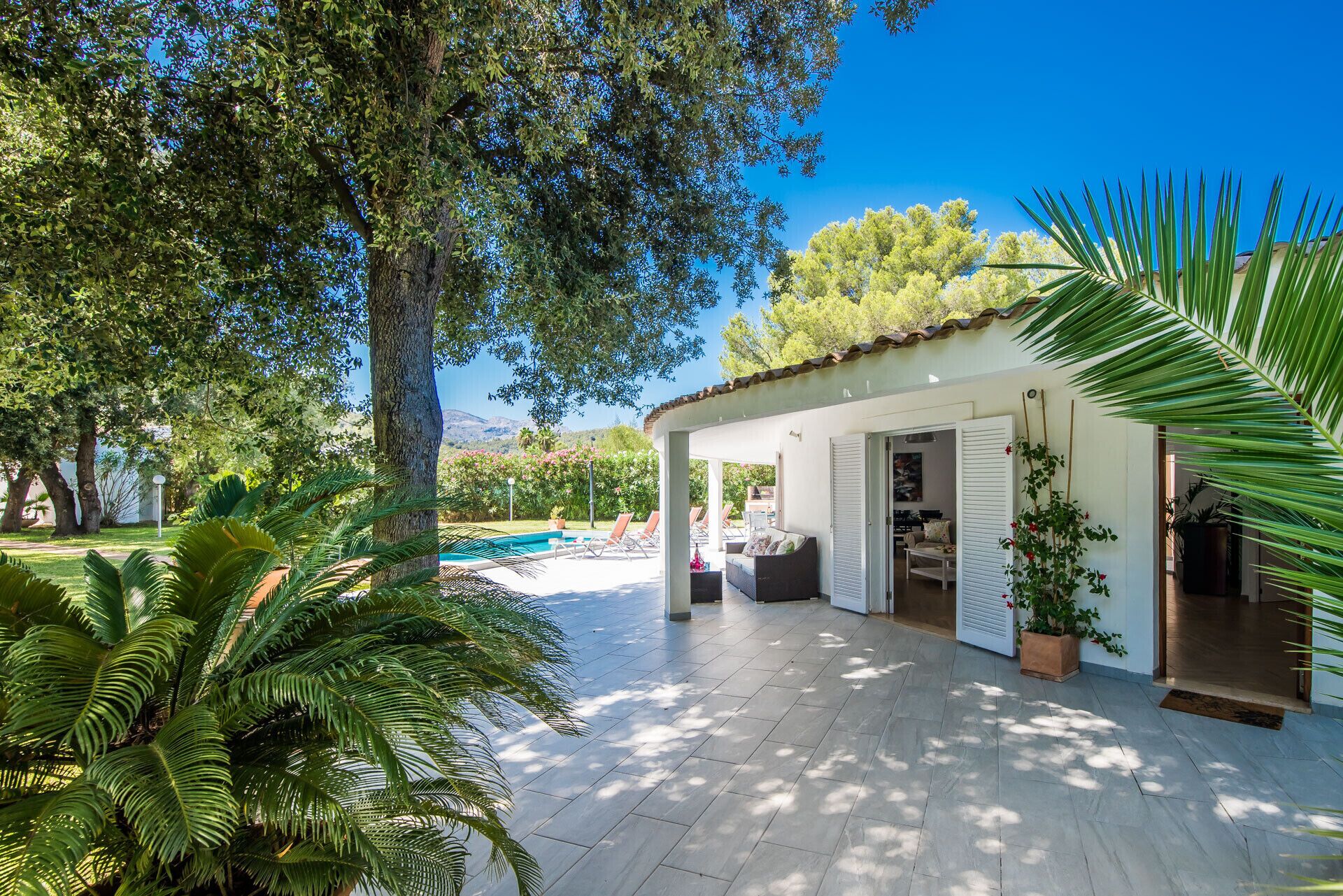 A covered outdoor area with a pool, surrounded by lush greenery and trees.