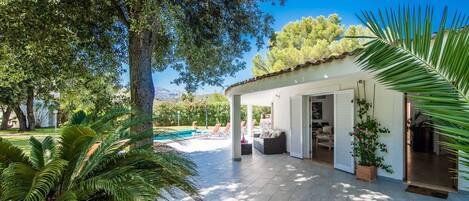 A covered outdoor area with a pool, surrounded by lush greenery and trees.