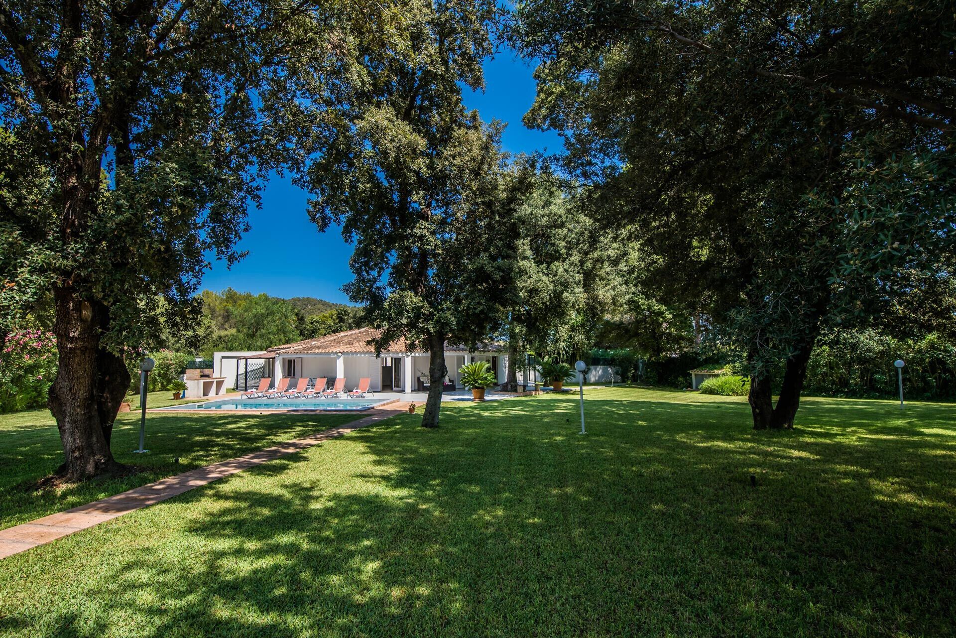 A pool area with lounge chairs, a building with a tiled roof, and a well-maintained lawn.
