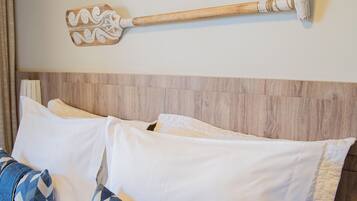 Un lit bien fait, avec des oreillers blancs et bleus à motifs, une tête de lit en bois et deux pagaies décoratives accrochées au mur au-dessus.
