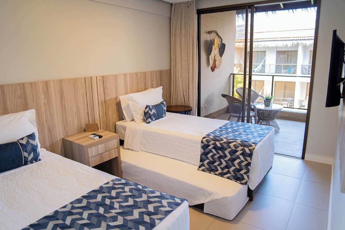 Ein Hotelzimmer mit zwei Betten, einem kleinen Tisch, einem Stuhl und einem Balkon mit Blick.