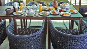 A dining area with tables set for breakfast, wicker chairs, and a thatched roof. - Porto das Dunas Boutique Praia Hotel (Aquiraz)
