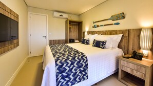A neatly made bed with a patterned bedspread, a bedside table with a lamp, and a wall-mounted TV. - Porto das Dunas Boutique Praia Hotel (Aquiraz)