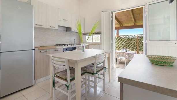 A modern kitchen with white cabinets, a stainless steel refrigerator, and a dining area with a table and chairs.