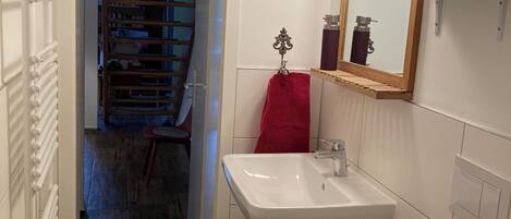 Une salle de bain avec un lavabo blanc, un miroir avec éclairage, une serviette rouge et une poubelle rouge.