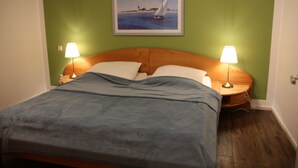 A neatly made bed with a blue blanket, two bedside lamps, and a framed picture of a sailboat on the wall. - Large, cozy vacation home in a quiet location (Groß Mohrdorf / Hohendorf)