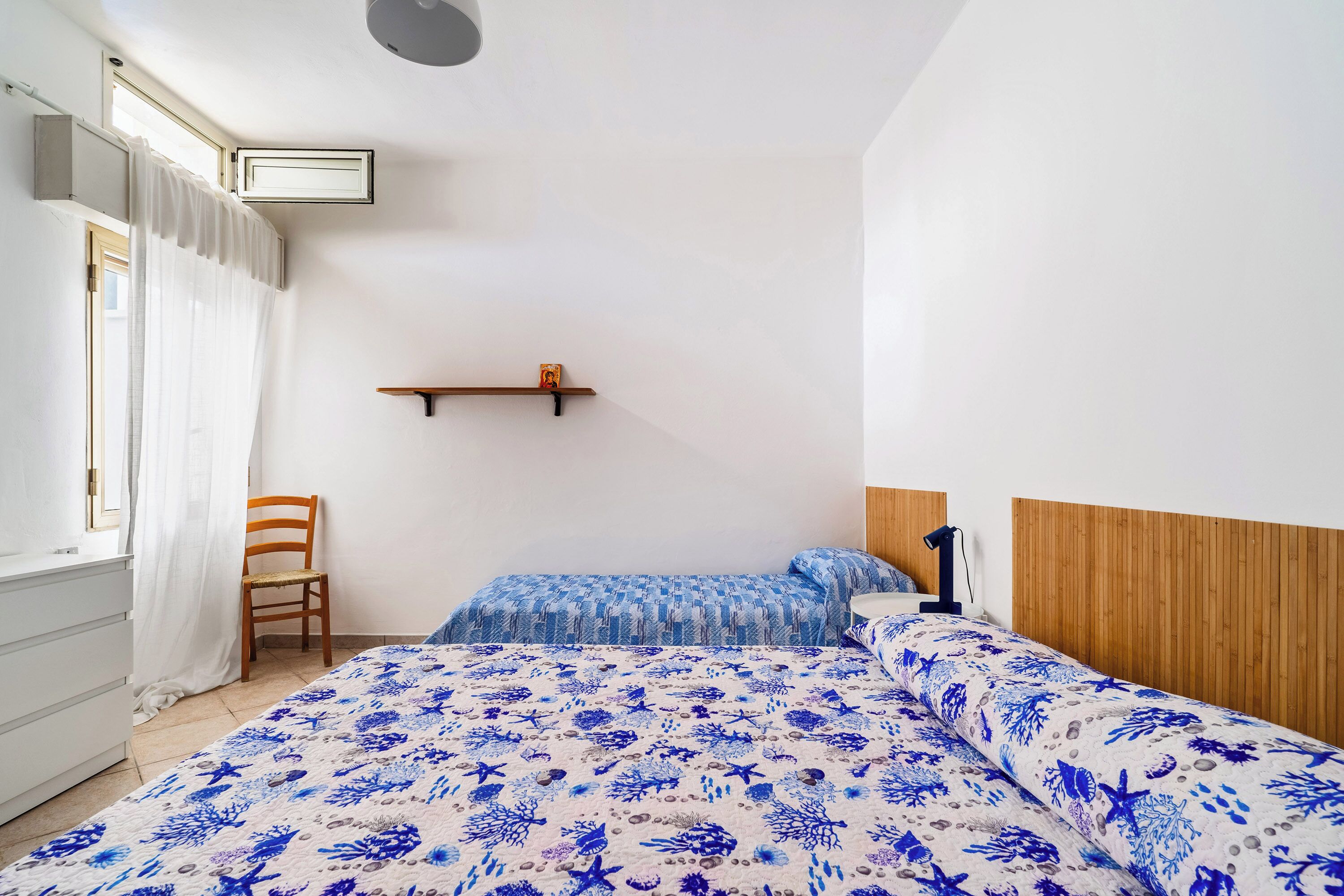 A bedroom with a bed, a chair, a shelf, and a window with curtains.