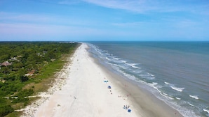 A wide beach with a clear view of the ocean, a sandy shoreline, and a line of trees and buildings along the coast.