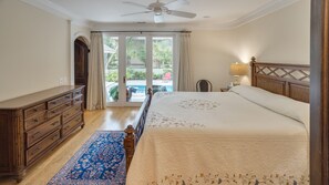 Un dormitorio con una cama grande, un aparador de madera, un ventilador de techo y vistas al exterior.