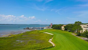 A coastal golf course with a lighthouse, marina, and historic buildings.