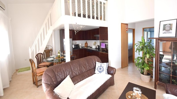 A spacious living area with a brown leather sofa, a dining table with chairs, a kitchen in the background, and a staircase leading to an upper level. - Holiday apartment with sea view (Pinezići/Krk)