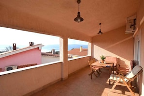 A balcony with a table and chairs, a hanging light fixture, and a view of the sea and mountains.