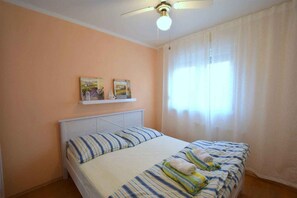 A bedroom with a bed, a ceiling fan, and a window with curtains.