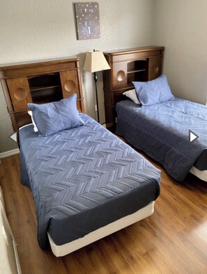 Two single beds with matching headboards and footboards, each topped with chevron-patterned bedding, are accompanied by a bedside table and lamp.