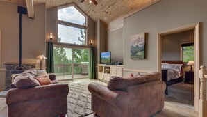 A spacious living room with a large window, a fireplace, and a television. - Treetop at Tahoe Donner By Tahoe Getaways - Dog OK - Access to Gym, Pool, Beach (Truckee)