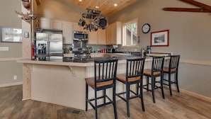 A kitchen with a central island, bar stools, wooden ceiling, and a clock on the wall. - Treetop at Tahoe Donner By Tahoe Getaways - Dog OK - Access to Gym, Pool, Beach (Truckee)
