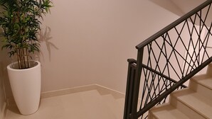 Un escalier avec une rampe en métal noir et un pot de plante blanche placé sur le côté gauche.