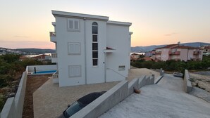Un bâtiment moderne de couleur blanche, doté d’une piscine, d’une voiture et offrant une vue sur les environs.