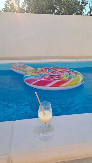 A swimming pool with a colorful inflatable structure and a glass of a yellow beverage. - New luxury apartment in villa with a pool (Okrug Gornji)