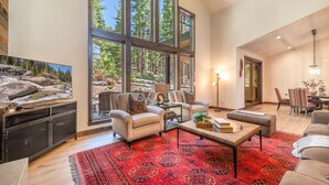 A spacious living room with large windows, a red patterned rug, and a television on a cabinet.