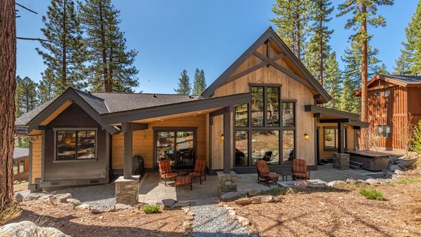 A modern log cabin with a covered patio, stone pathway, and outdoor seating area.