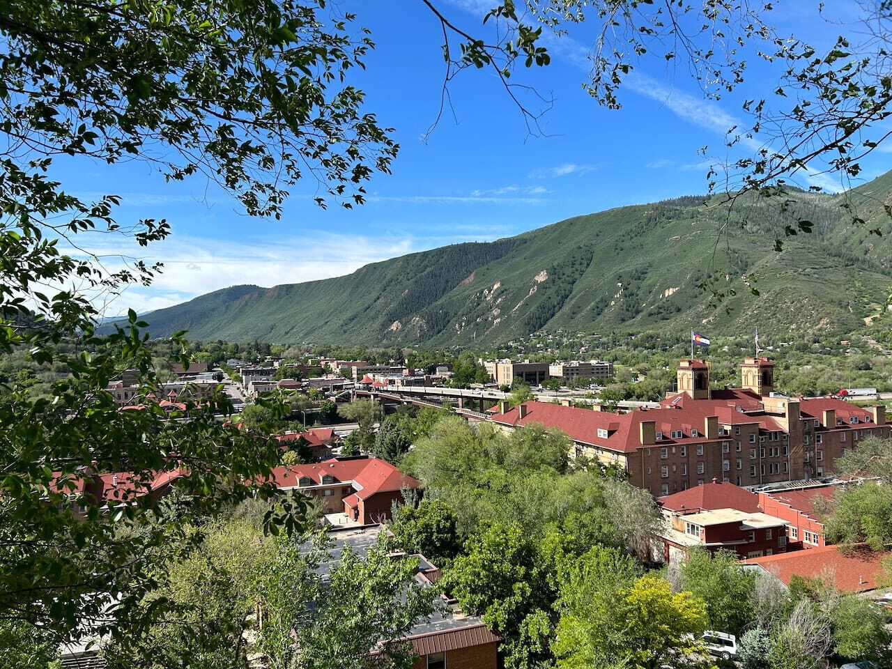 A town with red-roofed buildings, a bridge, and green hills in the background.