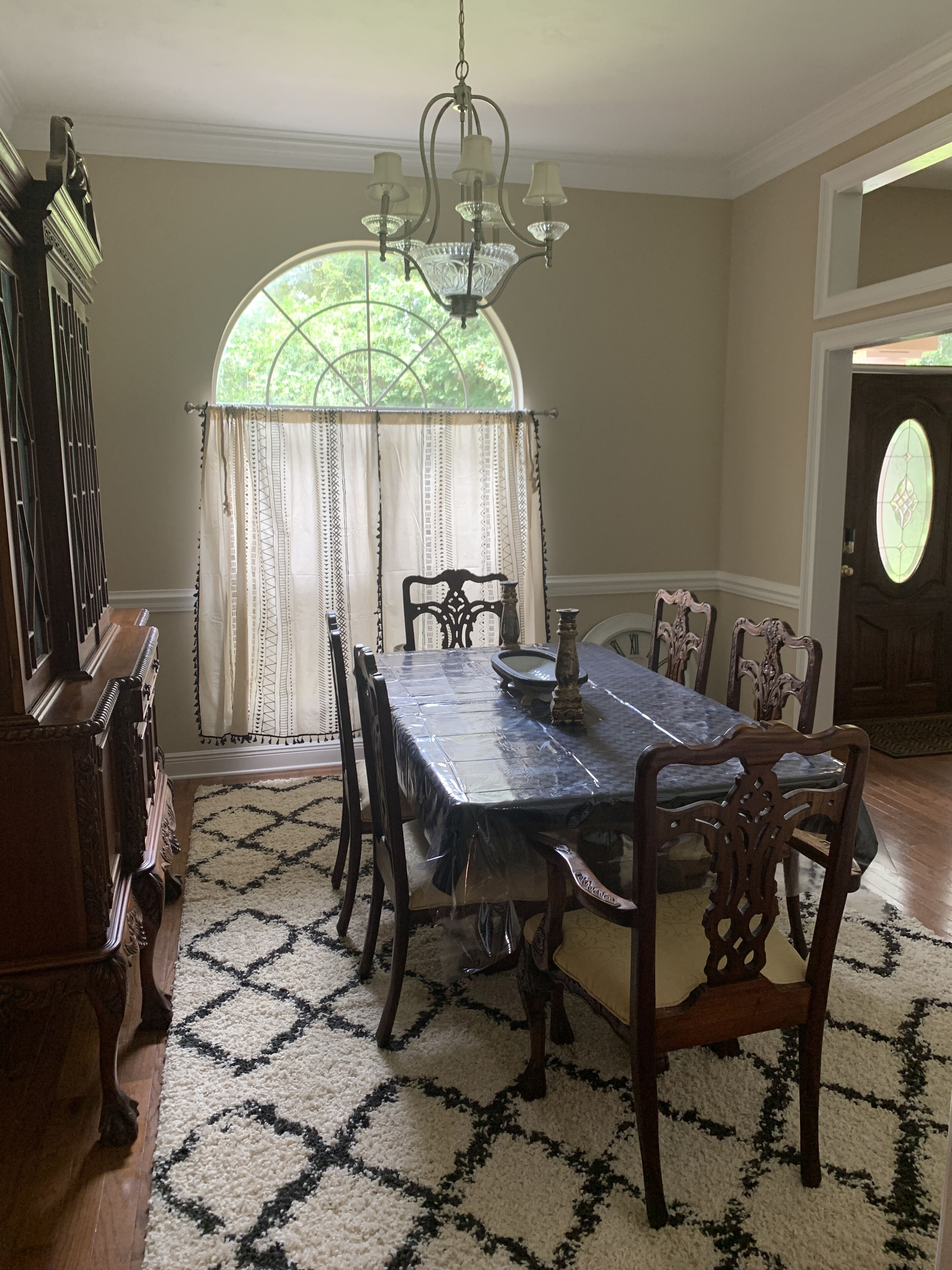 A dining room with a large table, chairs, a chandelier, and a window with curtains.