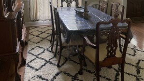 Un comedor con una mesa grande, sillas, una araña y un ventanal con cortinas.
