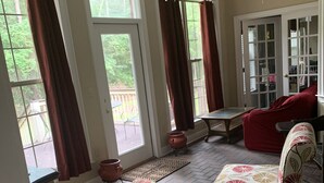 Amplia sala de estar con ventanas grandes, ventilador de techo y vista a una terraza de madera.