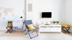 Un salon moderne avec un bureau blanc, une chaise bleue, un meuble de rangement blanc et un téléviseur à écran plat.