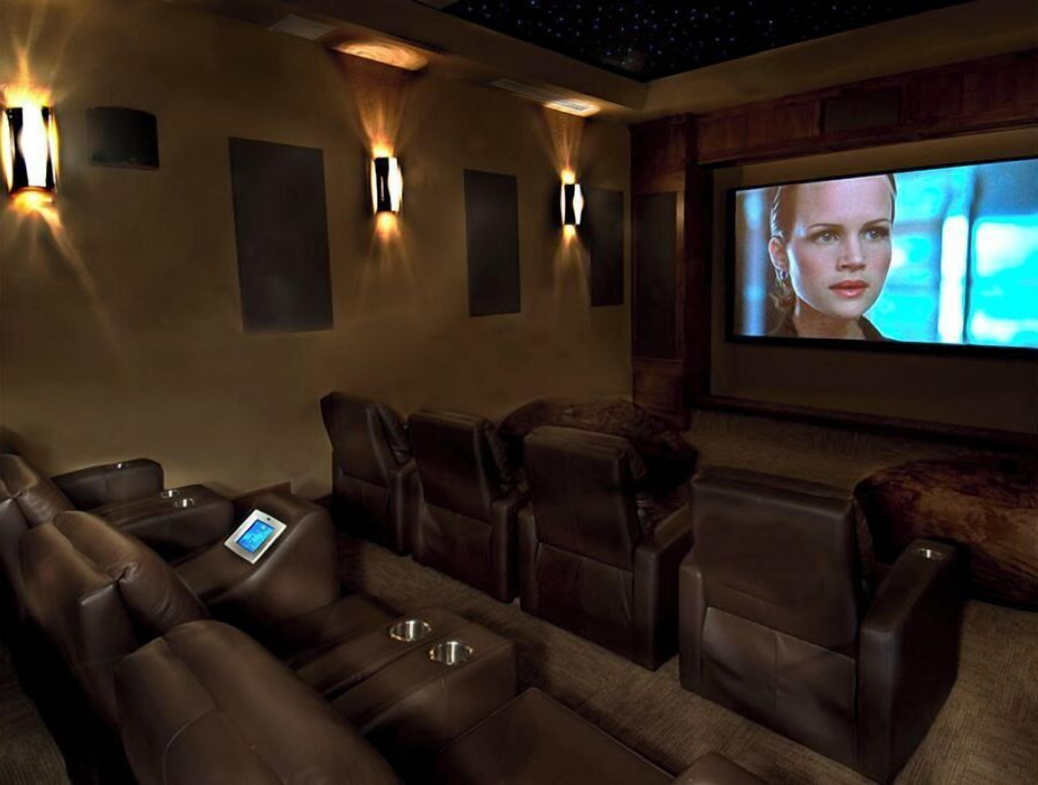 Ein Heimkino mit Ledersesseln, einem großen Bildschirm und Wandlautsprechern.