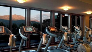 Une salle de sport équipée de tapis de course et d’appareils elliptiques, de grandes fenêtres offrant une vue sur les montagnes et de divers équipements d’exercice.