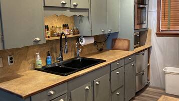 A kitchen with grey cabinets, a black sink, and a wooden countertop.