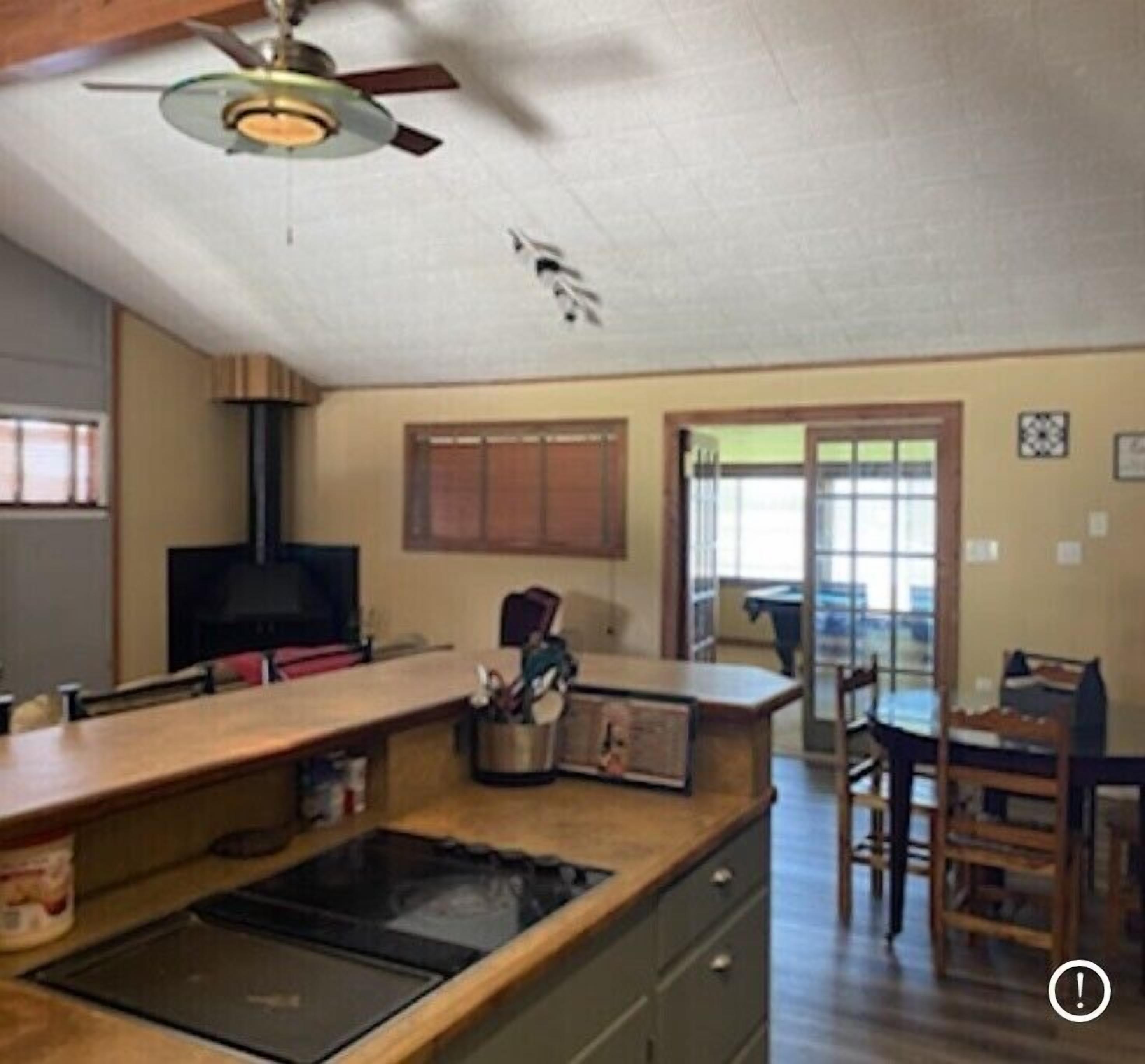 A kitchen with a central island, a stove, and a ceiling fan. There is a dining area with a table and chairs.