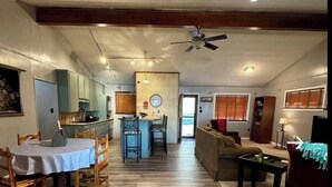 A spacious living area with a kitchen in the background, wooden flooring, and a ceiling fan. - Private lakefront home with amazing views! (Noble)
