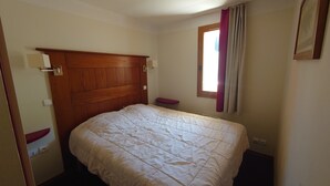 A bedroom with a wooden headboard, a single bed, a window with curtains, and a small shelf. - Apartment at the foot of the slopes in a typical village of our mountains (Les Coches, La Plagne-Tarentaise, France)