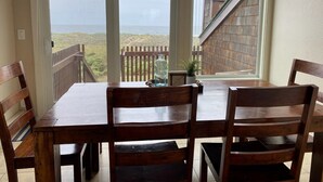 A wooden dining table with four chairs, a glass vase, and a small plant on the table. - Serene beachfront getaway, breathtaking ocean views, steps from the beach! (Moss Landing)