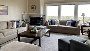 A living room with a fireplace, two sofas, a coffee table, and large windows. - Serene beachfront getaway, breathtaking ocean views, steps from the beach! (Moss Landing)