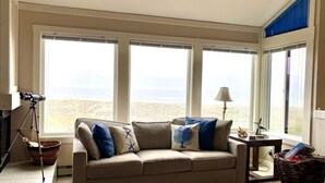 A living room with a beige sofa, a lamp, a telescope, and a view of the beach. - Serene beachfront getaway, breathtaking ocean views, steps from the beach! (Moss Landing)
