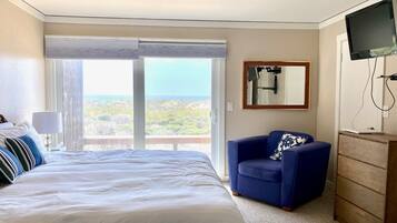 A hotel room with a large bed, a blue armchair, a wooden dresser, and a television.