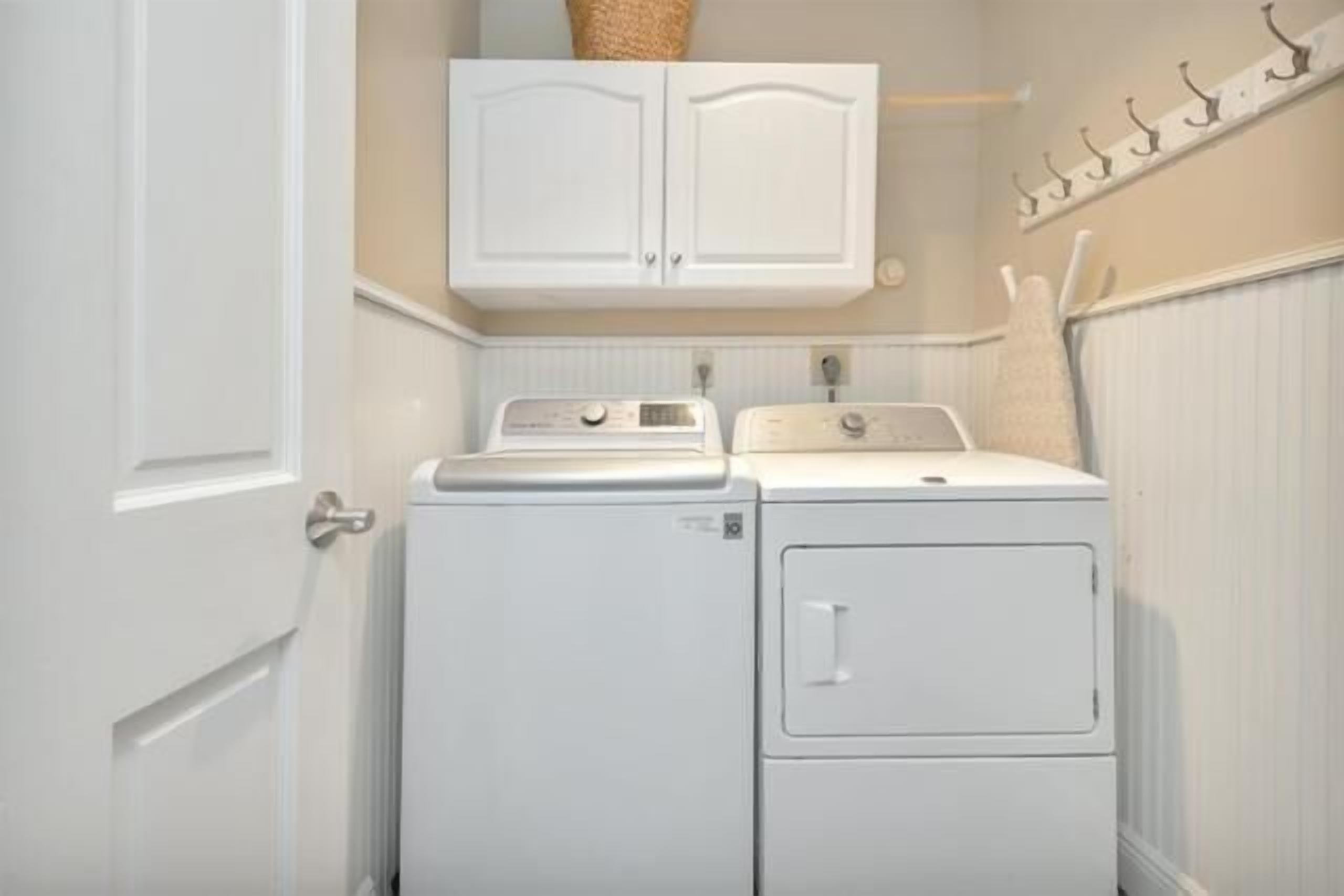 A laundry room with two stacked washers and dryers, a white cabinet above, and a towel rack on the wall.