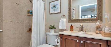 A bathroom with a shower, toilet, vanity, and a large mirror.