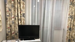 A living room with a flat-screen TV on a white cabinet, patterned curtains, and a herringbone-patterned floor. - Very nice luxury apartament (Varna)