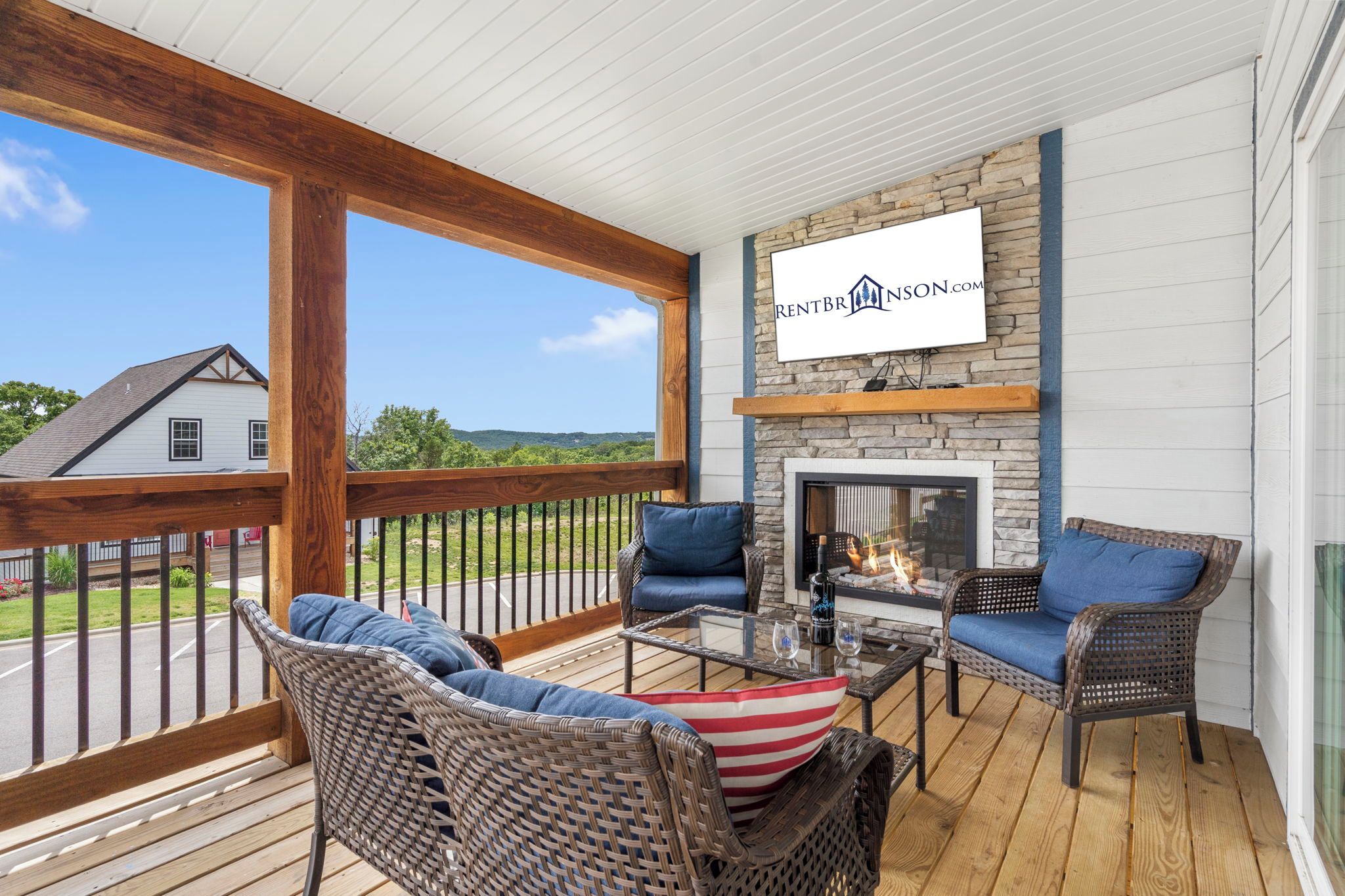 A covered outdoor seating area with wicker furniture, a fireplace, and a view of a house and landscape.