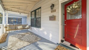A porch with a red door, a bench, and a rug.