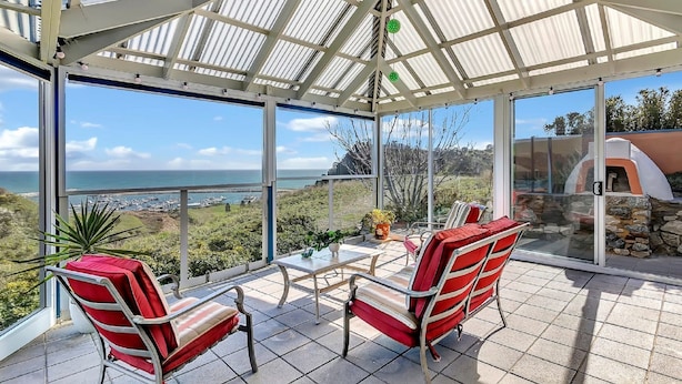 Veranda coperta con due sedie a righe rosse e un tavolo, con vista sulla costa.