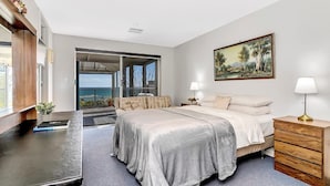 Una camera da letto con un letto, comodini, una cassettiera, un quadro e vista sul mare tramite un'ampia vetrata scorrevole.